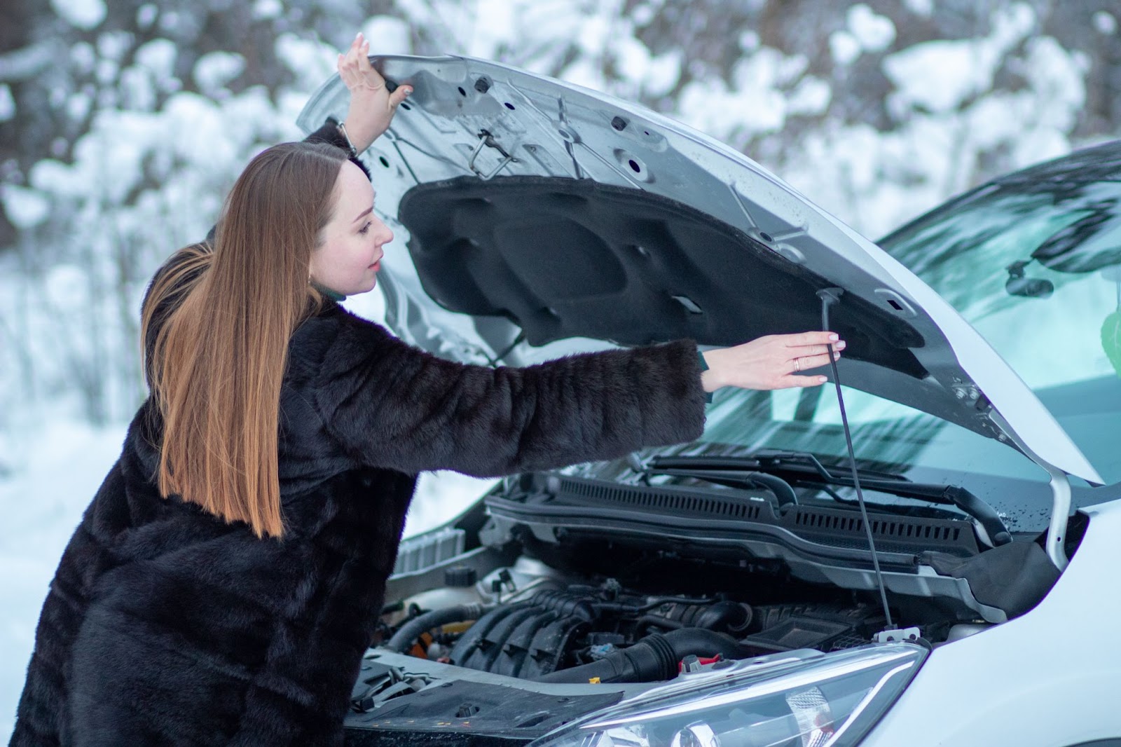 V zimě při nízkých teplotách nenechávejte auto stát celé týdny bez delší jízdy. | WebJET CMS Žena otevírá a podpírá kapotu auta v zasněženém prostředí.